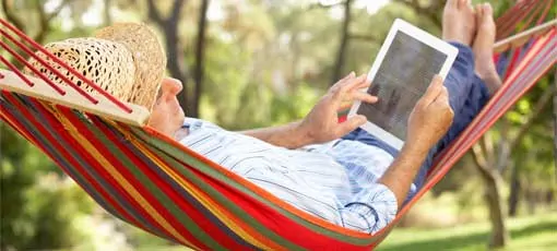 Ein Mann liegt in einer Hängematte und liest auf einem iPad